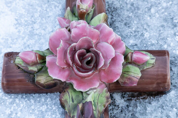 Pink ceramic rose on a brown cross memorial in winter snow