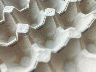 A top-down, close-up view of an empty grey molded pulp egg tray, showing a repetitive geometric pattern and textured paper surface.