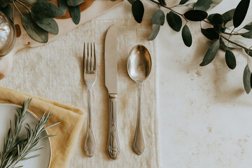 Elegant table setting with stainless steel cutlery fork knife and spoon on linen napkin with natural decor and rustic background