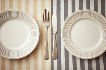 TMinimal table setting with empty ceramic plates fork and knife on striped textile background viewed from above