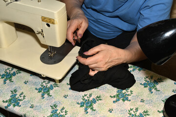 The seamstress sews together clothing pieces using a sewing machine.