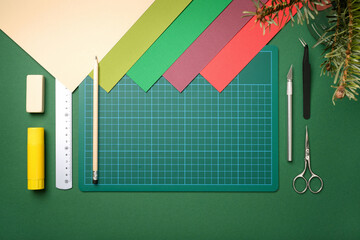 Top view of desk for paper crafts. Scissors, knife, pencil, glue, eraser, ruler, green cutting mat, colored paper. Space for your text.