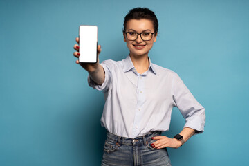 Portrait of gorgeous woman demonstrate smartphone display empty space isolated on blue color background