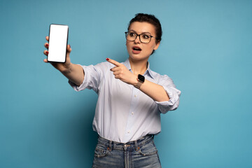 Portrait of gorgeous woman demonstrate smartphone display empty space isolated on blue color background