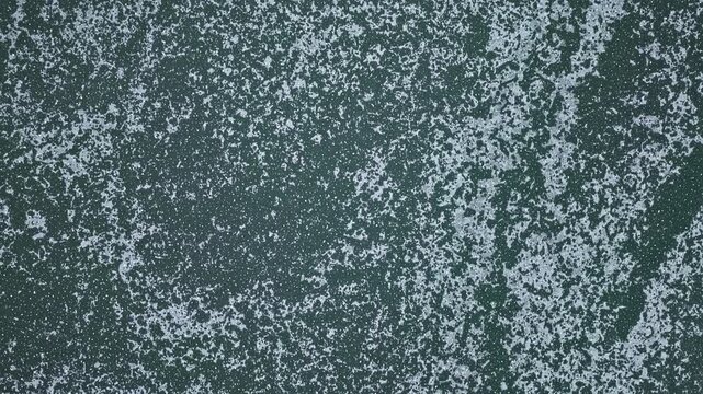 Top-down aerial drone view of a frozen lake surface with natural ice patterns and textures, winter background with calm and minimal atmosphere.