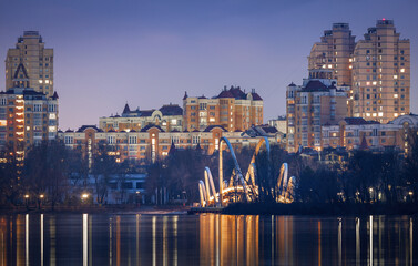 Night over Obolon embankment in Kyiv with modern residential skyline with lights reflected in calm river water, dramatic sky creating a peaceful urban evening atmosphere.a