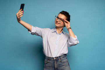 Middle aged woman laughing taking selfie photo isolated over blue