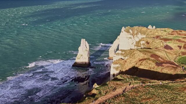 Pullout aerial of Falaise d'Aval showing white chalk sea cliffs, L'Aiguille needle natural arch in turquoise English Channel waters, and Cretaceous limestone geology in &Eacute;tretat, Normandy, France.