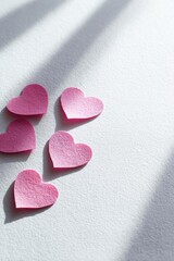 Obraz premium Pink paper hearts arranged diagonally on a white surface. Concept Pink paper hearts, Diagonal arrangement, White surface backdrop, Valentine’s craft decor, Paper art details