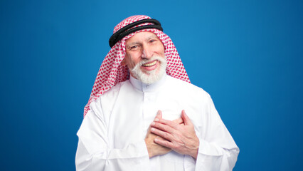 Senior muslim man wearing hijab talking gesturing, waving hand isolated on blue background