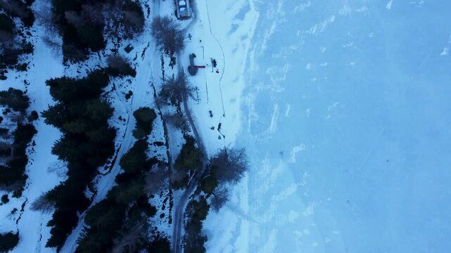 Top-down aerial drone footage of a frozen lake in Champex, Switzerland, with people ice skating in winter. Shot in 4K by a professional drone pilot using a DJI Mini 2.