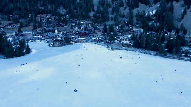 Aerial drone footage of Champex-Lac, Switzerland, showing a frozen alpine lake where people ice skate in winter. Snowy mountains and nature. Filmed in 4K with a DJI Mini 2.