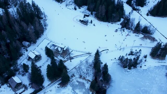 Aerial drone footage of a frozen lake in Champex, Switzerland, during winter. People ice skating surrounded by snowy alpine scenery. Shot in 4K using a DJI Mini 2.