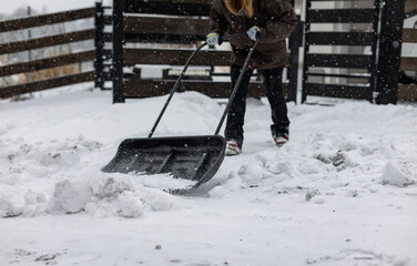 Large snow shovel in the hands of a woman clearing snow from her backyard