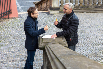 Two men discussing ideas while standing by a stone railing in a city setting