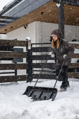 Large snow shovel in the hands of a woman clearing snow from her backyard