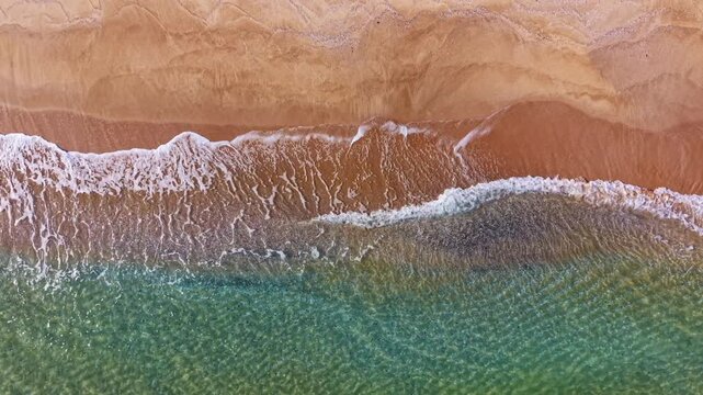 The tranquil ocean meets a golden sandy beach as gentle waves roll in, reflecting warm colors from the setting sun. Soft patterns form on the water's surface, evoking peace.