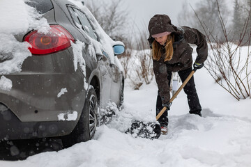 Woman with a snow shovel clears snow from a snow-covered car so she can drive out of the parking lot in front of her house