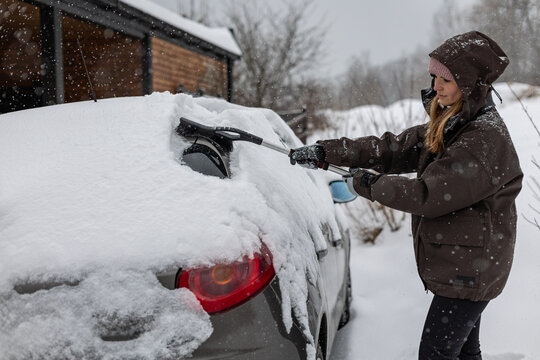 Woman clears snow from her car after a heavy snowfall using a snow brush