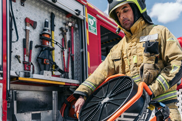 Obraz premium Firefighter holding ventilation fan at fire station with fire truck in background
