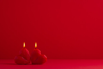 Two burning red heart shaped candles on red background. Valentine's day, 14 February. Love and romance.