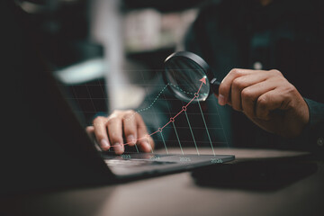 Businessman analyzing financial growth chart on laptop with magnifying glass from 2023 to 2026