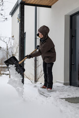 Snow shovel in the hands of a woman clearing snow from a snow-covered entrance to a house