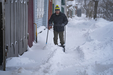 A man in a dark jacket shovels snow near a house, a village street, winter, snowdrifts