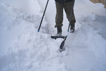Fototapeta premium A man in a dark jacket shovels snow near a house, a village street, winter, snowdrifts