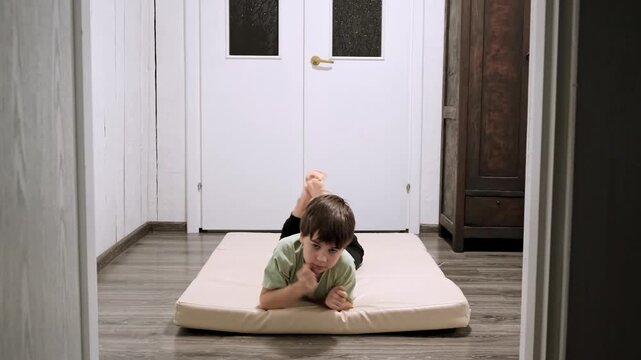 Caucasian boy doing a lying down sports exercise crawling on elbows by sports mat at home. Children workout. Happy child strengthening the muscles. The kid does a strong body. High quality 4k footage.