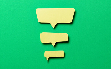 Yellow blank paper speech bubbles with shadow and copy space for text on green background, top view flat lay backdrop