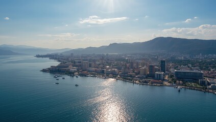 Fototapeta premium Aerial perspective of a coastal sea port featuring boats, urban structures, and mountain backdrop, highlighting maritime commerce