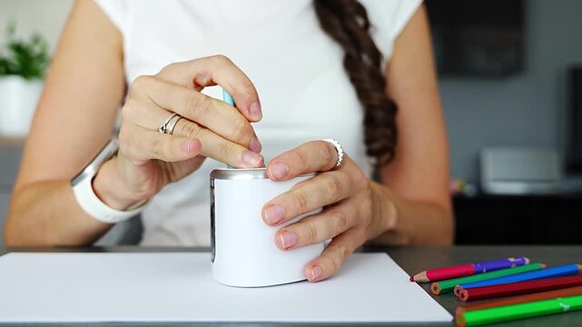 Close up of woman hands sharpening colored pencils with electric sharpener on desk in home office. Creative work process, preparation for drawing and everyday routine in real life workspace