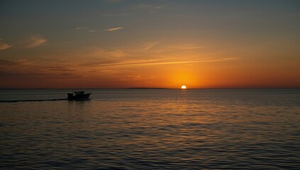 Naklejka premium Lone boat silhouette on the ocean at sunset with amber hues, highlighting peacefulness and isolation