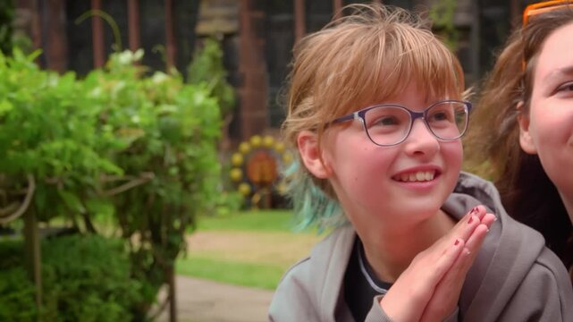 A young girl playfully puts her hands together in a mock prayer pose. She tries to stay serious but suddenly bursts into a fit of genuine laughter. A charming and funny moment of childhood joy