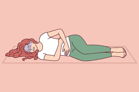 Female athlete lying on floor after workout holding her stomach in pain. Concept of endometriosis or digestive problems interrupting sports activity and healthy lifestyle