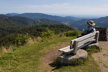 randonneur assis sur un banc au sommet du Ballon d'Alsace dans les Vosges en train d'admirer les paysages de for&ecirc;ts vosgiennes