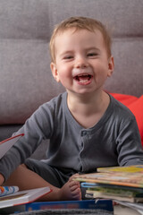 Cheerful toddler surrounded by stacks of books at home, representing curiosity, early childhood education, joyful learning, and playful discovery through reading.