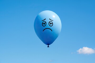 Blue Monday concept. Sad face balloon floating in clear blue sky, depression, mental health.
