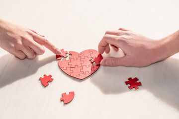 The hands of a woman and a man together create a heart from puzzle pieces. Relationship building, family, reconciliation, teamwork