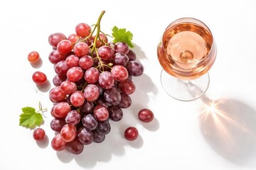 Top shot of ripe grapes alongside a rose wine glass on bright white backdrop