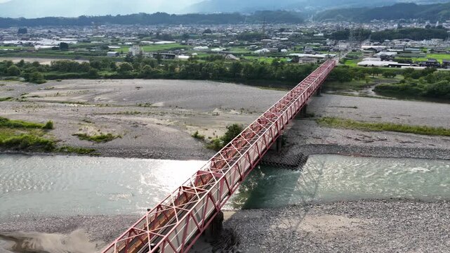 A red bridge spans a river, with a city in the background. The bridge is a large, red structure that spans the width of the river