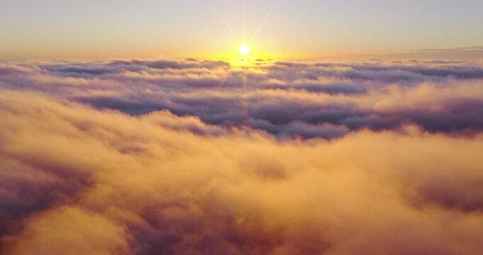 Aerial flight above glowing clouds at sunset with golden sunlight breaking through. Cinematic skyscape with soft fog, warm colors and dramatic atmosphere high above the horizon.