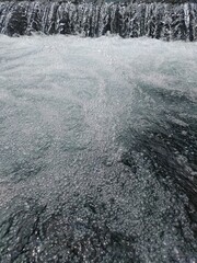 Close Up Foamy Waterfall Flow over Dark River Rocks Texture