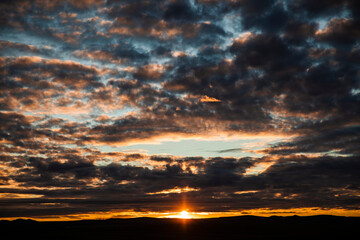 Dramatic cloudy sky during sunset with layered clouds and warm evening colors. Atmospheric nature background with abstract sky textures.
