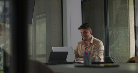 Young man celebrates success at laptop with joyful reaction during quiet office work session, smiling and cheering alone in modern workspace