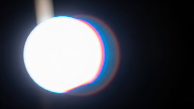 Bright light bulb emits warm glow in dark space with colorful lens flare effects - Powered by Adobe