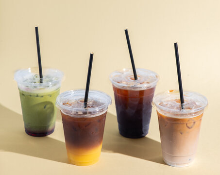 Assorted iced beverages including iced coffee, matcha latte, orange coffee, and iced cappuccino served over ice in clear takeaway cups. Modern cafe drink selection photographed on a clean, minimal stu