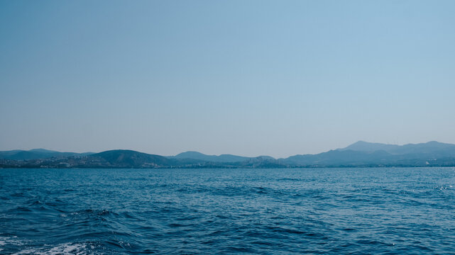Vast blue ocean waters with distant rolling mountains under a clear sky on a bright day