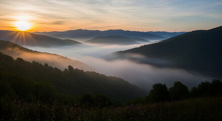 A scenic mountainous landscape at dawn, with sunburst, low-lying fog, silhouettes, and shades of green